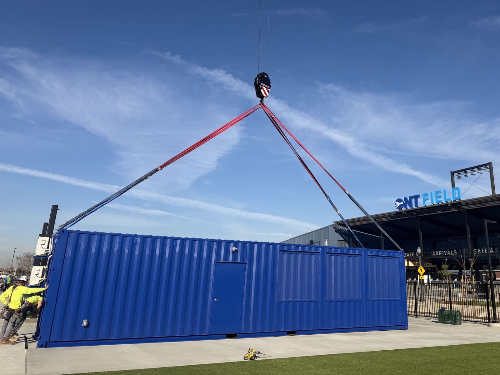 Blue container retail unit being craned into place outside a ballpark